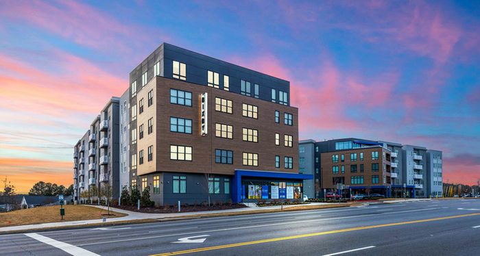 Modern apartment building with sleek design, captured during a stunning sunset on a spacious street corner.