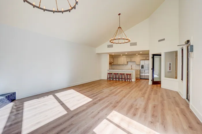 Bright open-concept living space featuring high vaulted ceilings, elegant chandeliers, and a modern kitchen with bar seating.