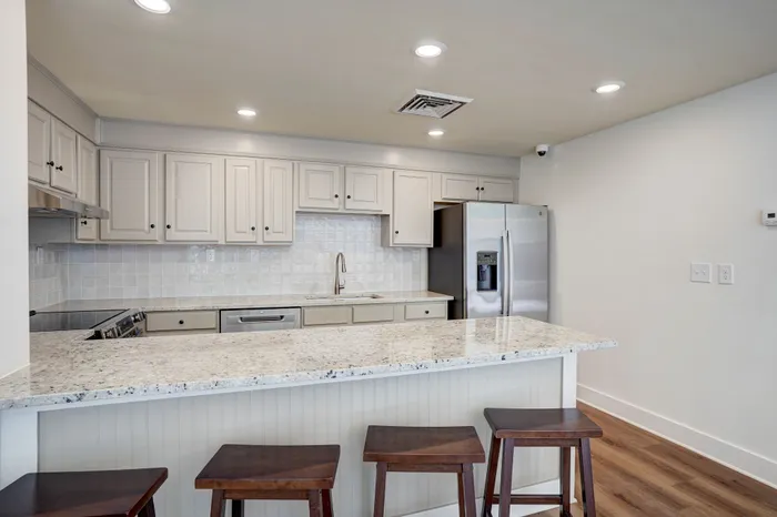 Modern kitchen with sleek granite countertops, elegant cabinetry, and stainless steel appliances. Inviting breakfast bar with wooden stools creates a welcoming space for casual dining.