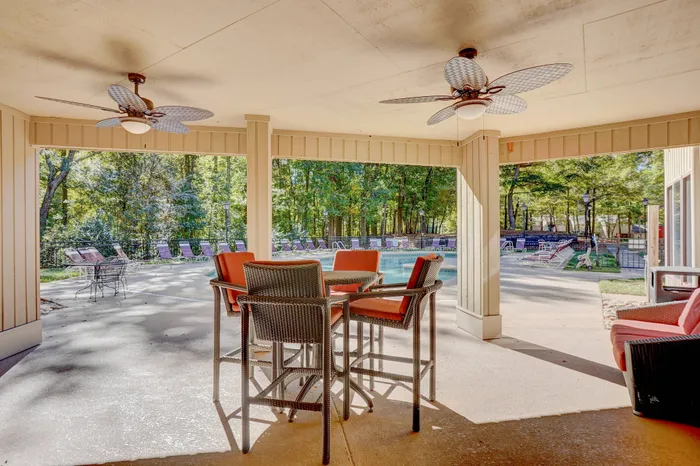 Chic outdoor lounge with stylish wicker furniture and ceiling fans, overlooking a serene pool area surrounded by lush greenery.