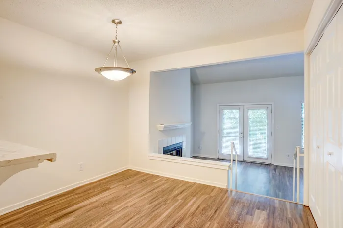Bright and inviting open-concept area with elegant wood flooring, modern lighting, and large double doors leading to a sunlit patio.