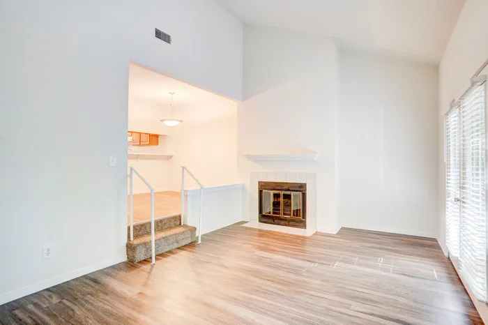 Bright and airy apartment showcasing a cozy living area with a modern fireplace, elegant light fixture, and steps leading to a charming kitchen space.
