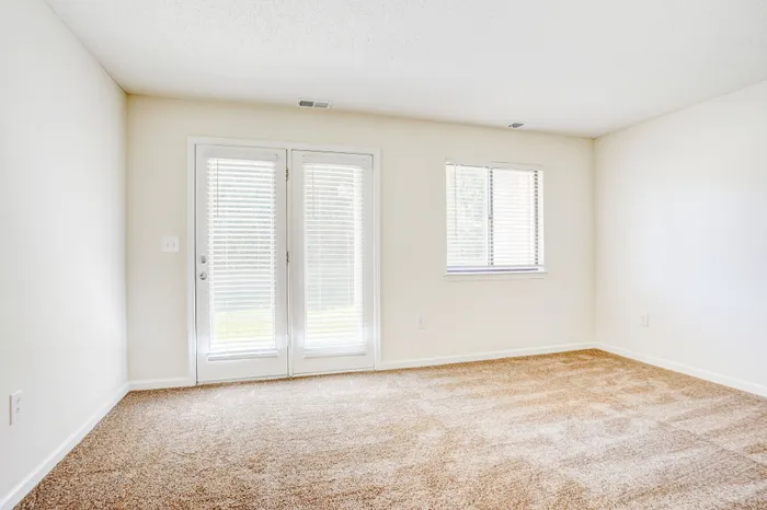 Bright and airy room with plush carpet, large double doors, and a window, perfect for a cozy retreat.