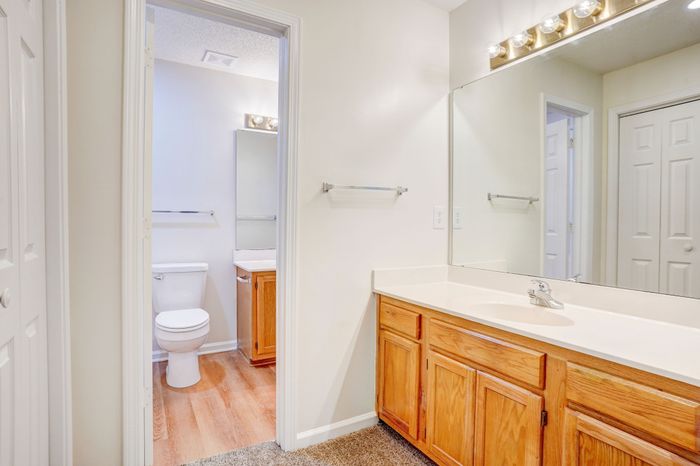 Bright and inviting bathroom with wooden cabinets, elegant lighting, and a large mirror, showcasing modern simplicity.