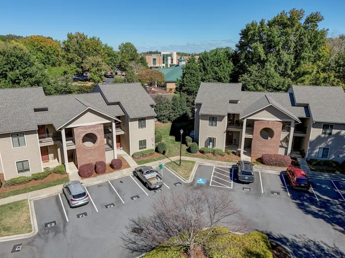Charming apartment complex with modern architecture, surrounded by lush greenery and ample parking space.