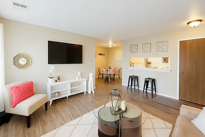 Bright and modern living room with sleek hardwood floors, cozy seating, and a stylish open kitchen with a breakfast bar, leading to a charming dining area.