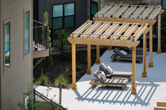 Wheatfield Village Apartments Courtyard Pool Lounge Seating Pergola. Enjoy a relaxing day by the pool, lounging on comfortable seating under the shaded pergola in the beautiful courtyard of Wheatfield Village Apartments.