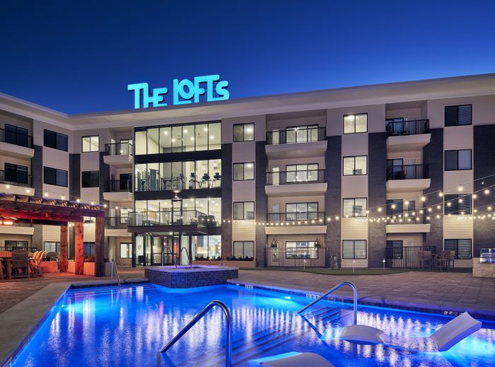 The Lofts at City Center exterior at dusk with illuminated windows" Caption: "Welcome home to modern urban living