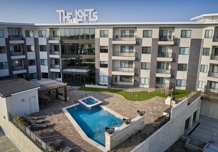 The Lofts at City Center exterior with rooftop signage and private balconies" Caption: "Your landmark address in Lenexa City Center