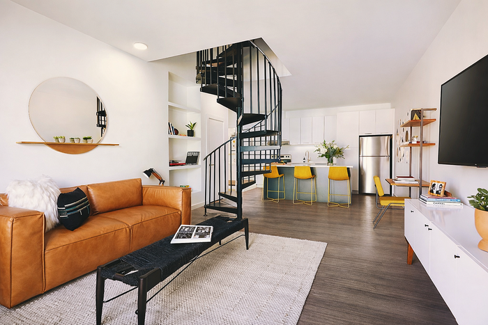 Modern apartment interior showcasing a chic spiral staircase, sleek kitchen with yellow bar stools, and cozy living area with a leather sofa.