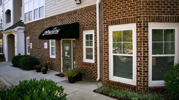 Charming brick apartment exterior with lush greenery and inviting entryway, showcasing warm hospitality and style.