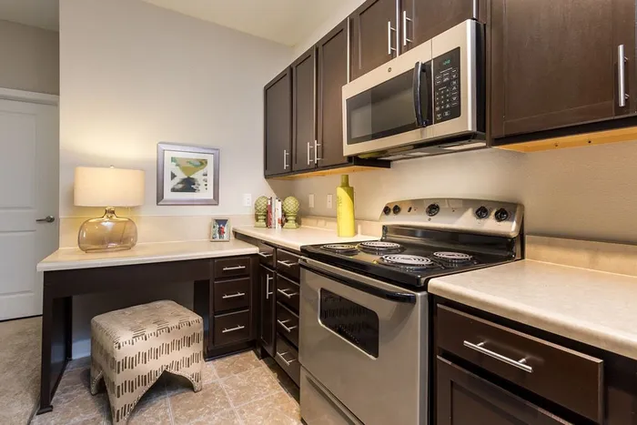 Elegant kitchen with modern appliances, sleek dark cabinets, and cozy workspace with a stylish ottoman.