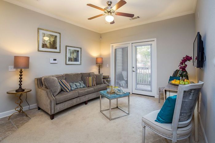 Inviting living room with plush sofa, stylish art, and vibrant decor creating a cozy ambiance. Features modern furniture, soft lighting, and large glass doors for natural light.