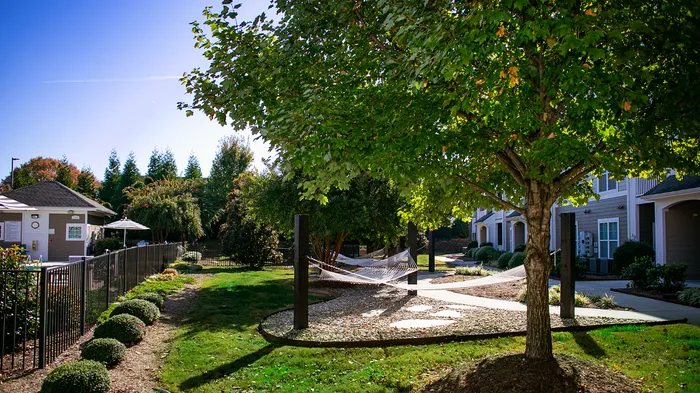 Tranquil apartment complex courtyard featuring cozy hammocks under lush trees, surrounded by well-manicured gardens and modern architecture.