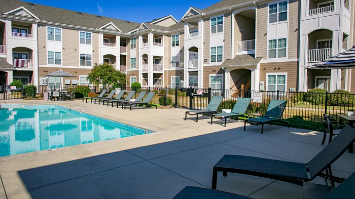 Charming apartment complex with modern architecture, featuring a sparkling pool and comfortable lounge chairs under clear blue skies.