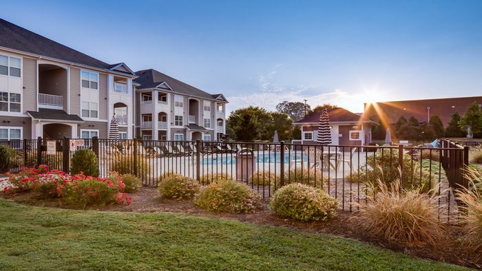 Charming apartment complex with modern design, featuring a refreshing outdoor pool, vibrant landscaping, and inviting balconies under a clear blue sky.
