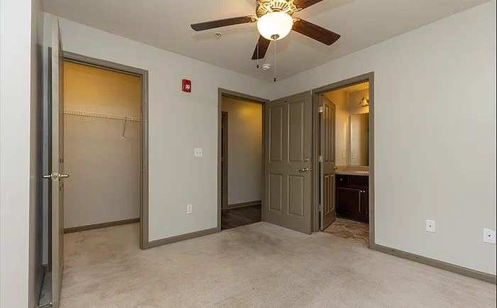 Inviting bedroom with plush carpet, ceiling fan, and convenient closet space, leading to a modern bathroom.