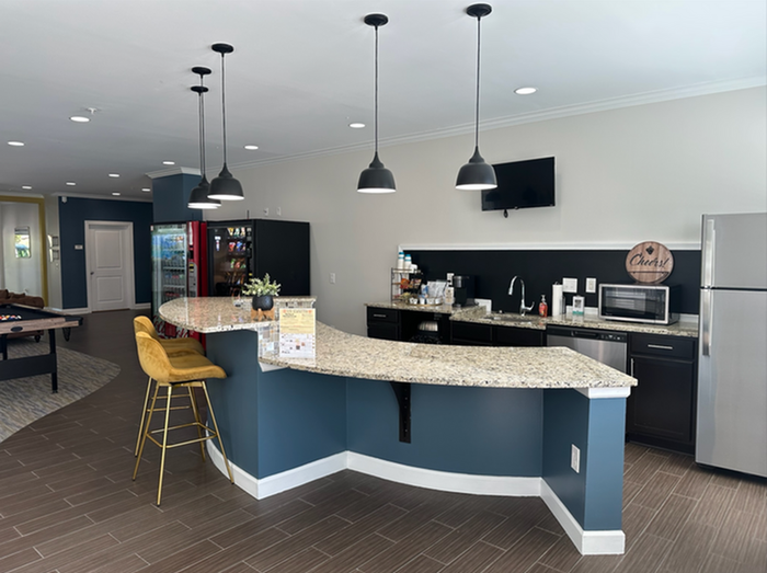 Contemporary community space with a sleek granite countertop bar, stylish pendant lighting, stainless steel appliances, and inviting barstool seating.
