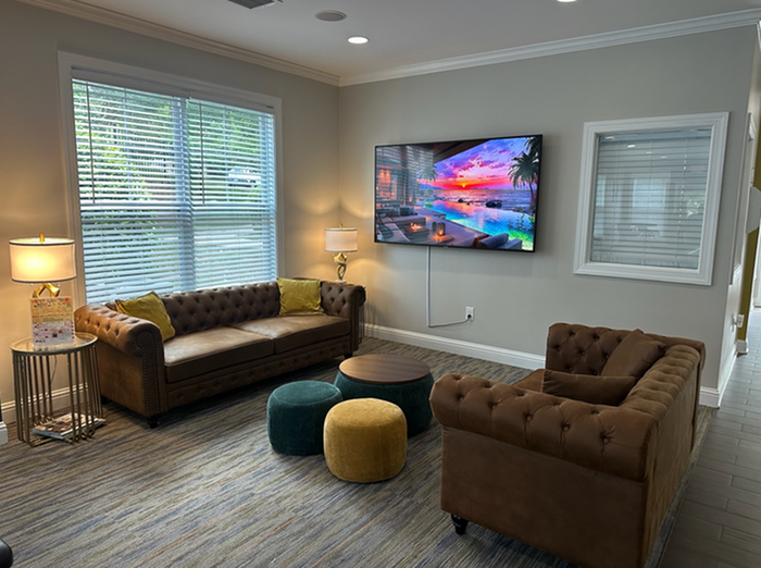 Inviting living room with elegant tufted sofas, vibrant poufs, and a large TV displaying a stunning sunset, perfect for relaxation and entertainment.