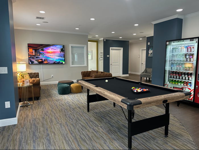 Chic apartment lounge boasting a modern pool table, cozy seating, vibrant decor, and a stocked beverage fridge.