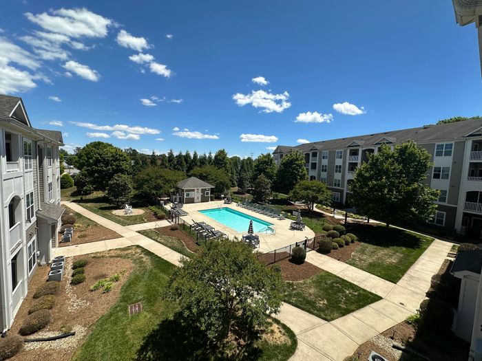 Inviting apartment complex featuring a sunlit courtyard and sparkling swimming pool surrounded by lush greenery and modern buildings.