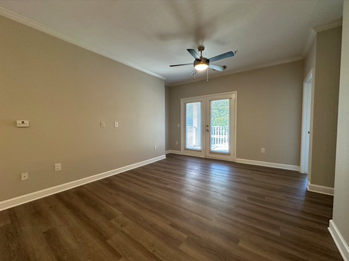 Bright living room with elegant wood flooring, modern ceiling fan, and glass doors leading to a serene balcony.
