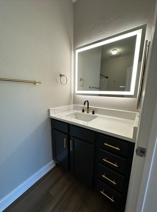 Sleek and modern bathroom with elegant vanity, illuminated mirror, and brass fixtures.