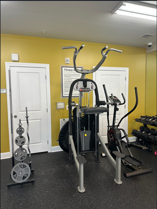 Bright and inviting gym space featuring modern fitness equipment including weights, an elliptical, and a multi-use machine, accented by a vibrant yellow wall.
