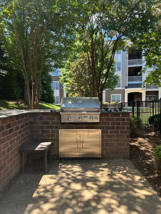 Charming outdoor barbecue area surrounded by lush greenery, perfect for al fresco dining at a modern apartment complex.