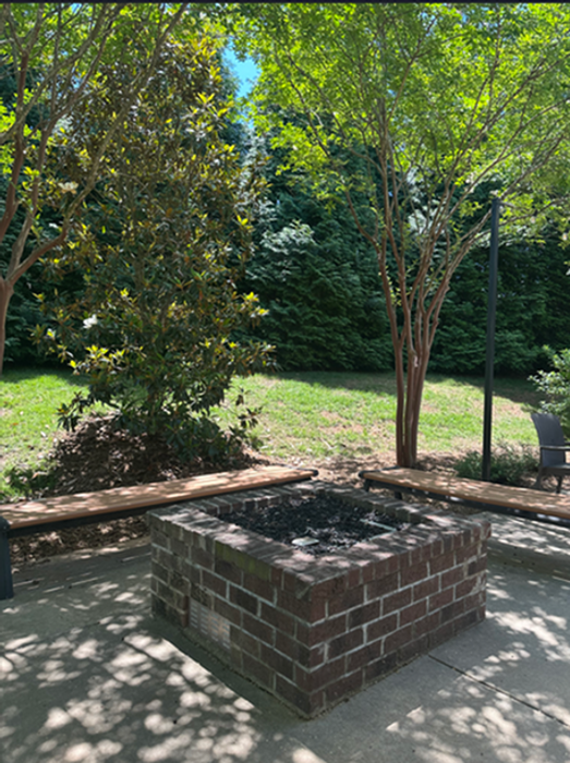 Charming outdoor patio with a brick fire pit surrounded by lush greenery and wooden benches, perfect for cozy gatherings.