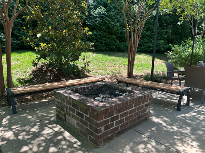 Charming outdoor space with a cozy brick fire pit, surrounded by benches and lush greenery, offering a serene retreat.