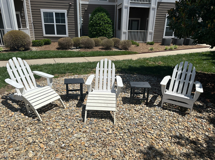 Charming outdoor seating with white Adirondack chairs on a stone patio, nestled against a vibrant garden backdrop in a modern apartment setting.