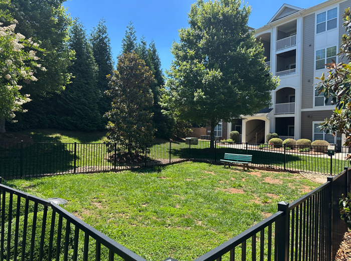 Charming apartment complex with lush green lawns, shaded benches, and fenced garden area perfect for relaxation.