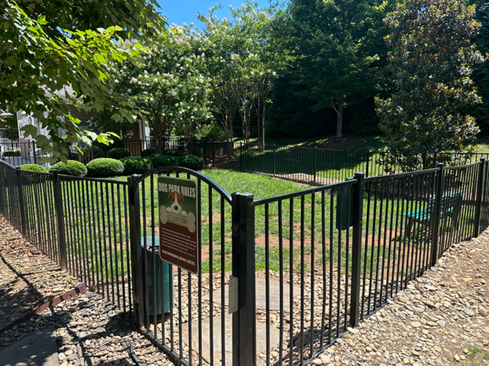 Inviting fenced dog park with lush greenery and shaded areas, perfect for pet-friendly living.