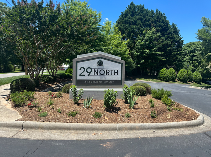 Inviting entrance to 29 North Apartment Homes with lush greenery and a welcoming sign.