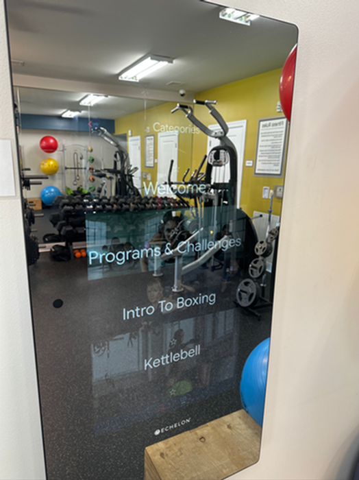 Vibrant gym space featuring modern fitness equipment, colorful exercise balls, and digital programs like Intro to Boxing and Kettlebell.