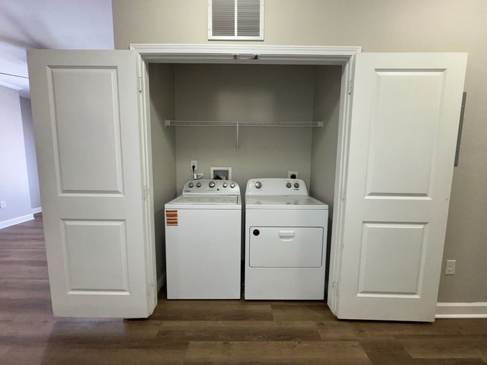 Convenient in-unit laundry area with modern washer and dryer in a stylish open closet, featuring elegant wood flooring.