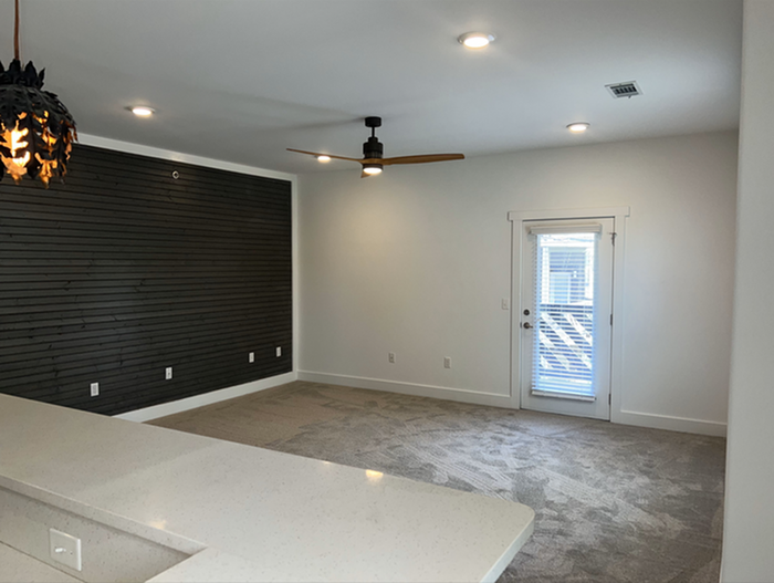 Modern living area with sleek wood accent wall, plush carpet, and stylish ceiling fan, offering a cozy yet contemporary vibe.