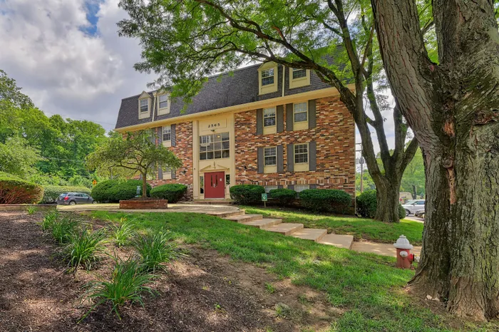 Charming three-story apartment building with a classic brick exterior, nestled within lush greenery and mature trees, offering a serene and inviting atmosphere.