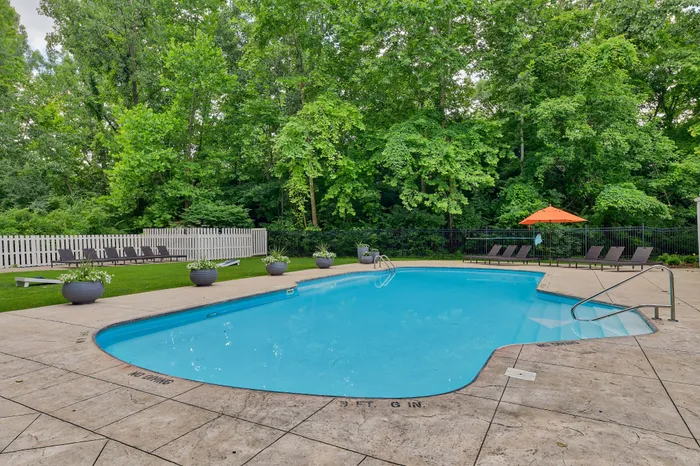 Inviting swimming pool area surrounded by lush greenery, featuring comfortable lounge chairs and vibrant umbrellas for a relaxing retreat.