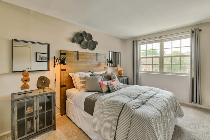Inviting bedroom filled with natural light, featuring a cozy bed with plush pillows, stylish wooden decor, and large windows offering lush green views.