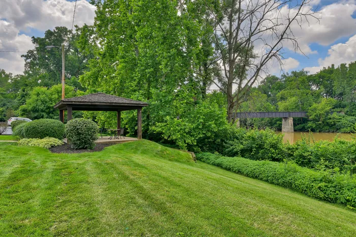 Charming outdoor gazebo set amidst lush greenery with a serene riverside view.