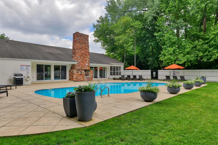 Inviting outdoor pool area with lush greenery, stylish lounge chairs, and vibrant orange umbrellas, perfect for relaxation and entertaining.
