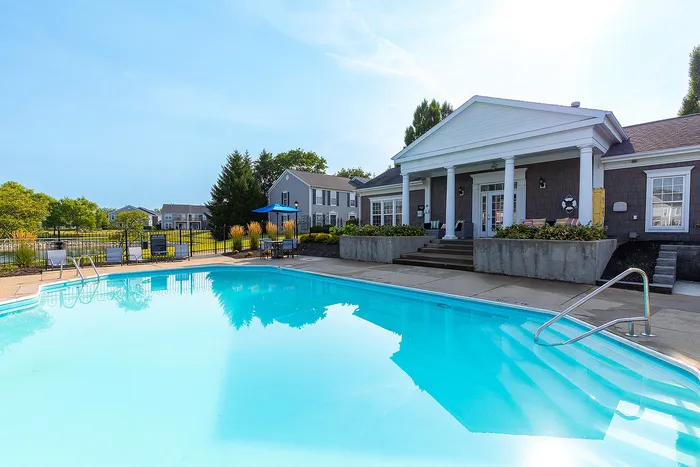 Charming residential clubhouse featuring a sparkling swimming pool, inviting outdoor seating, and lush greenery under a clear blue sky.