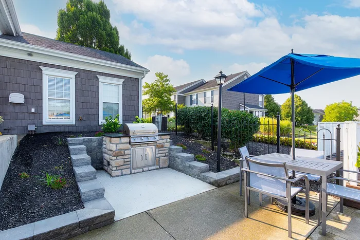 Chic outdoor patio with a sleek stone grill and stylish seating under a vibrant blue umbrella, perfect for entertaining.