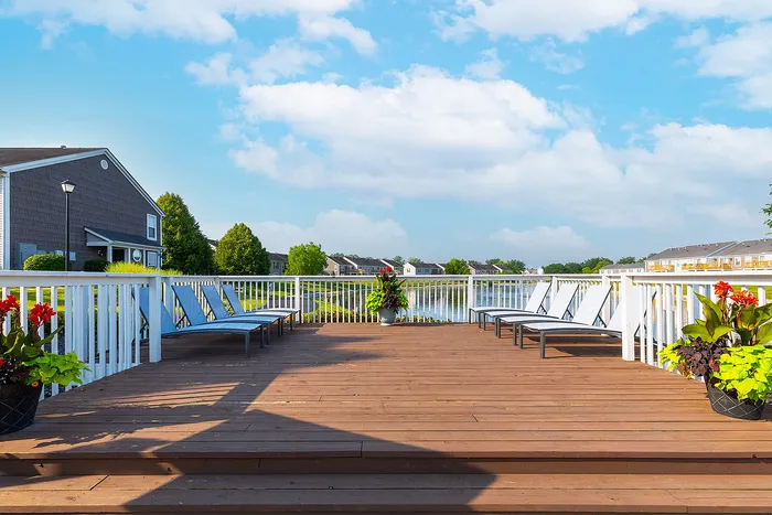 Inviting wooden deck with modern loungers, vibrant potted plants, overlooking a serene pond and lush greenery.