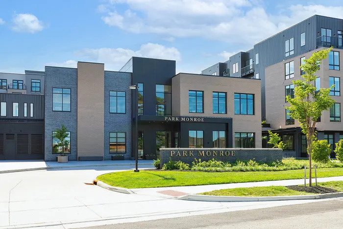Modern apartment complex with sleek architecture at Park Monroe, surrounded by lush greenery and expansive blue skies.