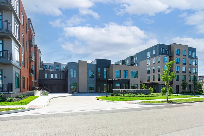 Modern apartment complex with stylish architecture, featuring large windows and lush landscaping on a sunny day.