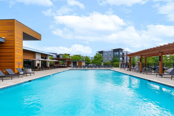 Luxurious apartment complex featuring a sparkling outdoor pool surrounded by modern architecture and comfortable lounge chairs, perfect for relaxation.