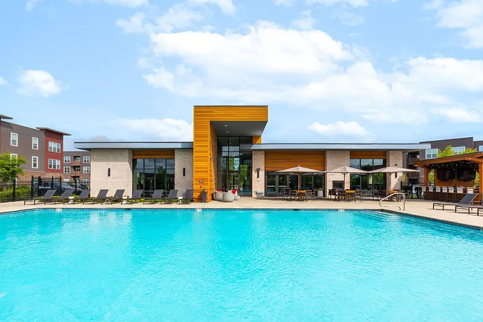 Luxurious apartment complex featuring a sparkling blue pool, stylish lounge chairs, and inviting outdoor seating under elegant canopies.